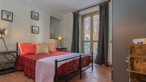 Una camera da letto con un letto, un comodino, una lampada, una finestra con tende e un armadio in legno.