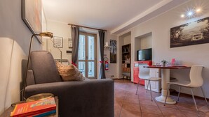 Un accogliente soggiorno con un divano, un tavolino e una libreria. C'è anche un'area pranzo con tavolo e sedie, e un televisore montato a parete.