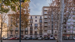Un edificio residenziale a più piani con balconi, auto parcheggiate e foglie autunnali a terra.