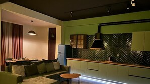 A modern living room with a green sofa, a small round table, and a kitchen area with green cabinets and a herringbone-patterned backsplash. - Luxury apartments by city (Baku)