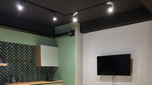 A modern living room with a green sofa, a wooden coffee table, and a herringbone-patterned floor. A flat-screen TV is mounted on the wall, and there is a kitchen area with green cabinets and a herringbone backsplash. - Luxury apartments by city (Baku)