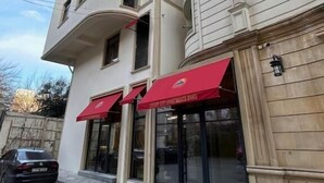A multi-story building with a modern facade, featuring large windows and a red awning with signage. - Luxury apartments by city (Baku)