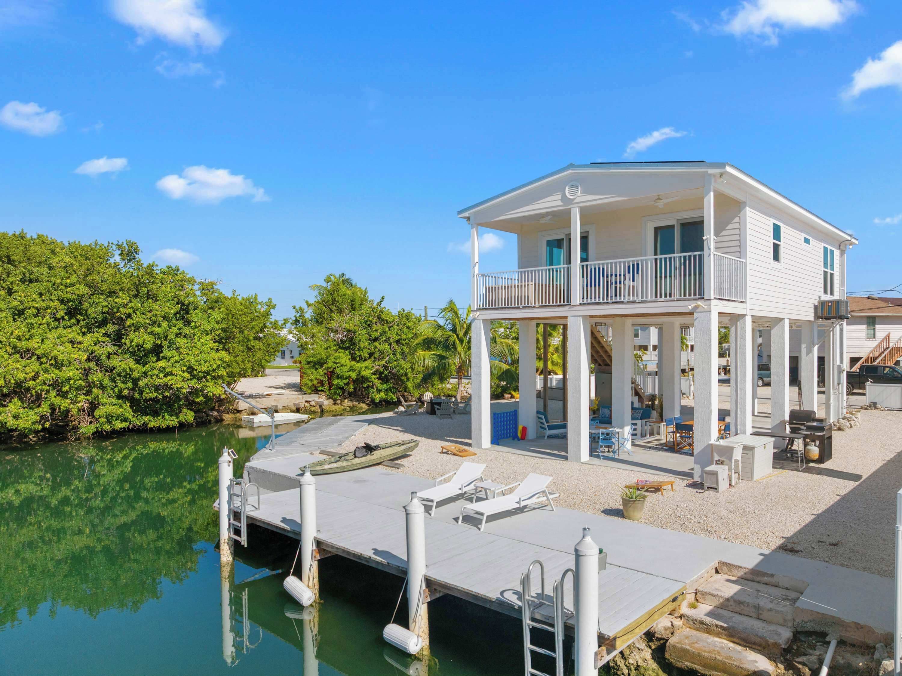 A two-story waterfront house with a balcony, dock, and outdoor seating area.