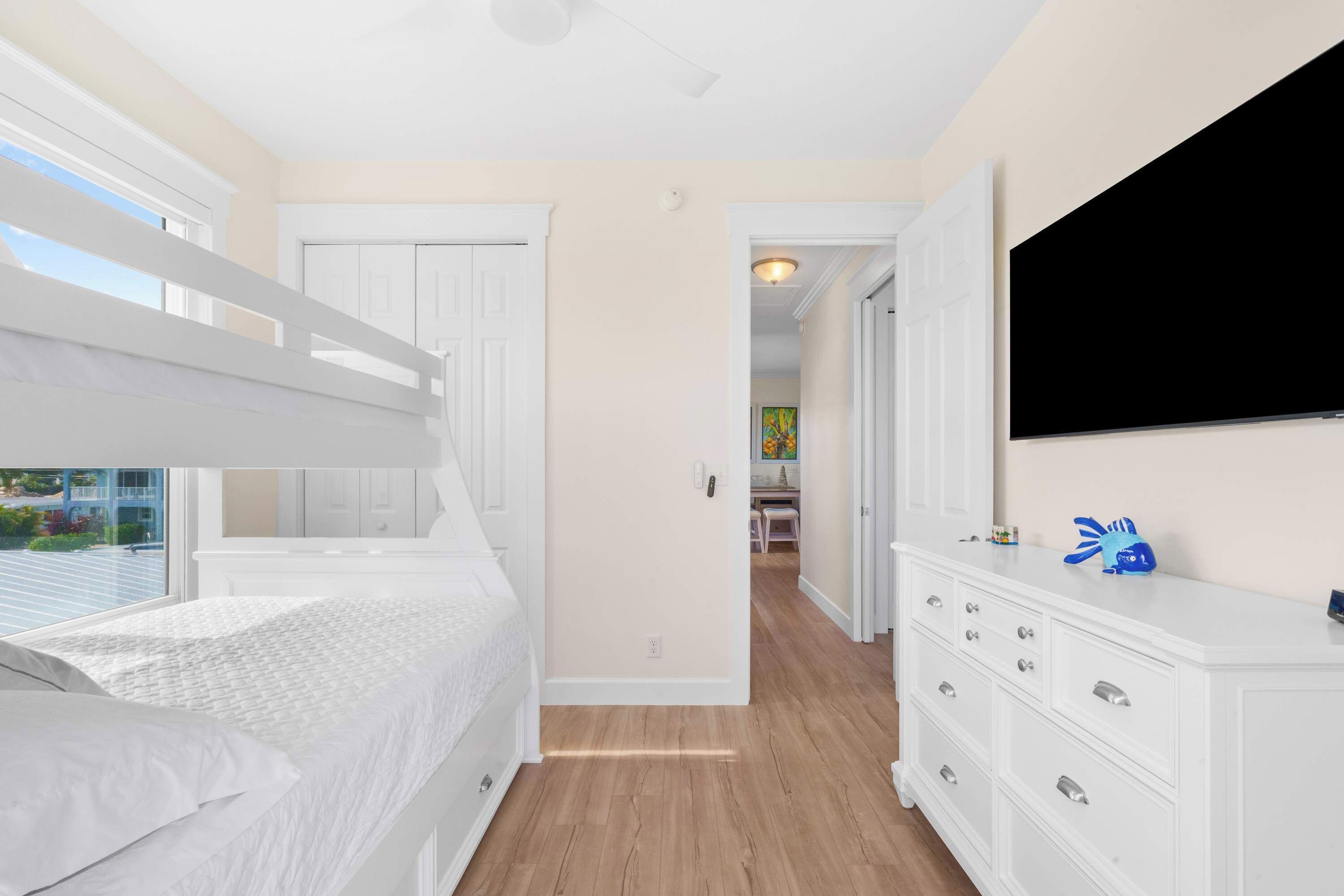 Een slaapkamer met een stapelbed, een witte dressoir en een flatscreen televisie.