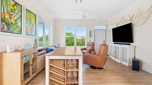 Een ruime woonkamer met een houten salontafel, een leren bank, een aan de muur bevestigde televisie en een groot raam met uitzicht op het omliggende landschap.