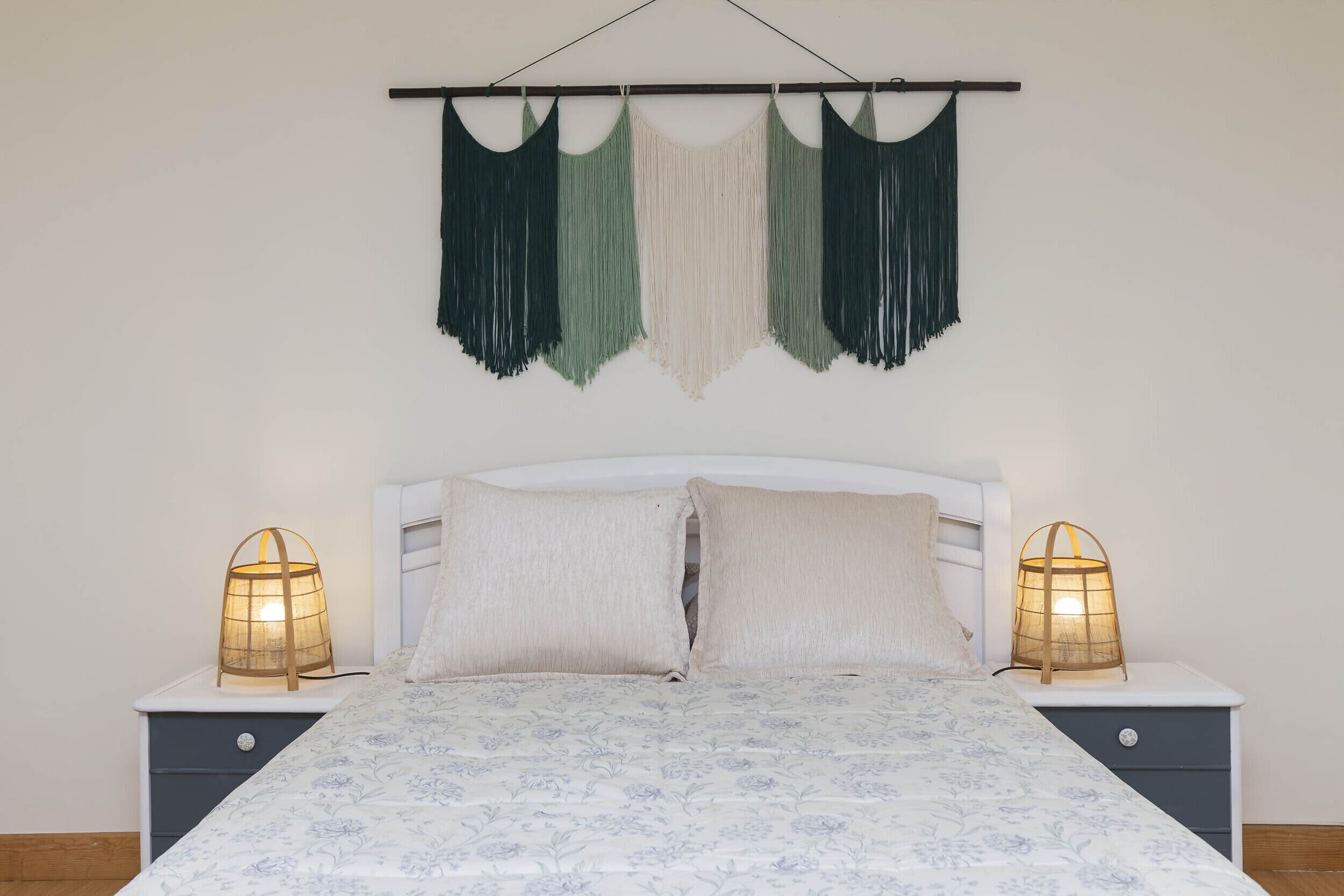 Un lit recouvert d’une couvre-lit à motifs floraux, deux lampes de chevet et une décoration murale en macramé.