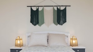 Een bed met een bloemenbedekking, twee bedlampjes en een macramé wanddecoratie.