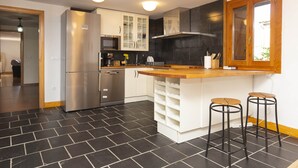 Een moderne keuken met een roestvrijstalen koelkast, witte kastjes, een houten aanrecht en twee barkrukken.