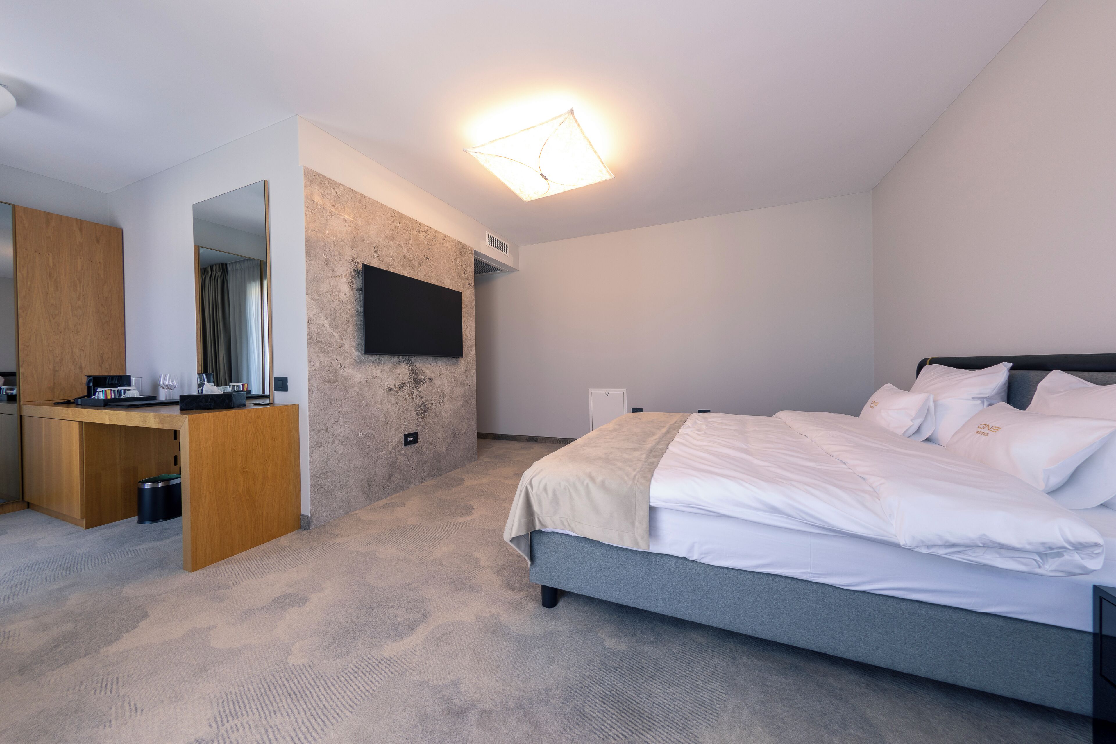 Un dormitorio moderno con cama, escritorio y televisor en la pared.