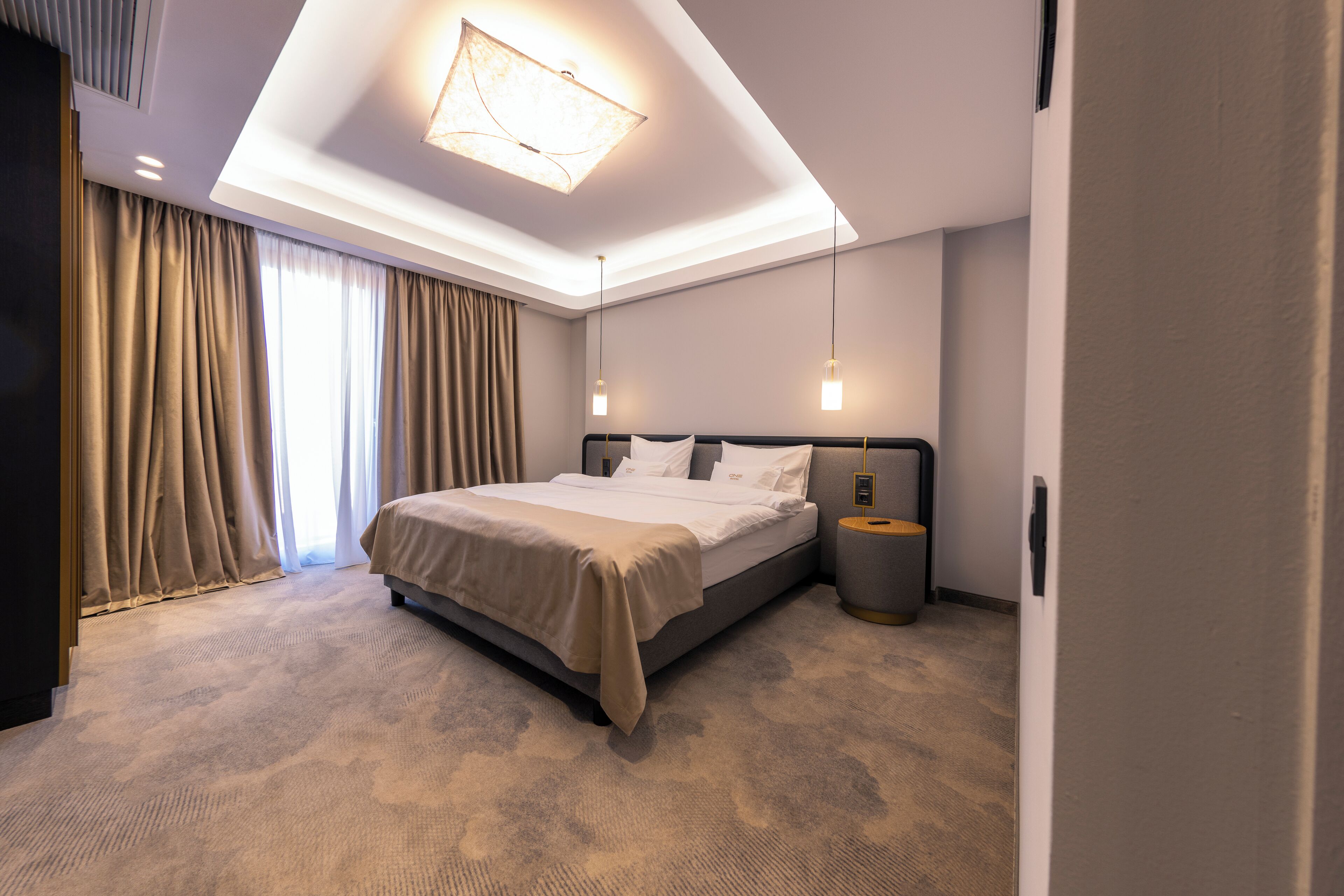 Une chambre moderne avec un grand lit, une table de chevet, une commode et un luminaire au plafond.