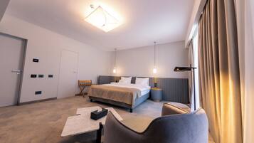 Habitación de hotel con cama, mesitas de noche, escritorio, silla y un amplio ventanal con cortinas.