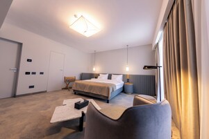 Habitación de hotel con cama, mesitas de noche, escritorio, silla y un amplio ventanal con cortinas.