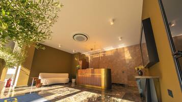 A modern lobby with a reception desk, a sofa, a potted plant, and a large mirror.