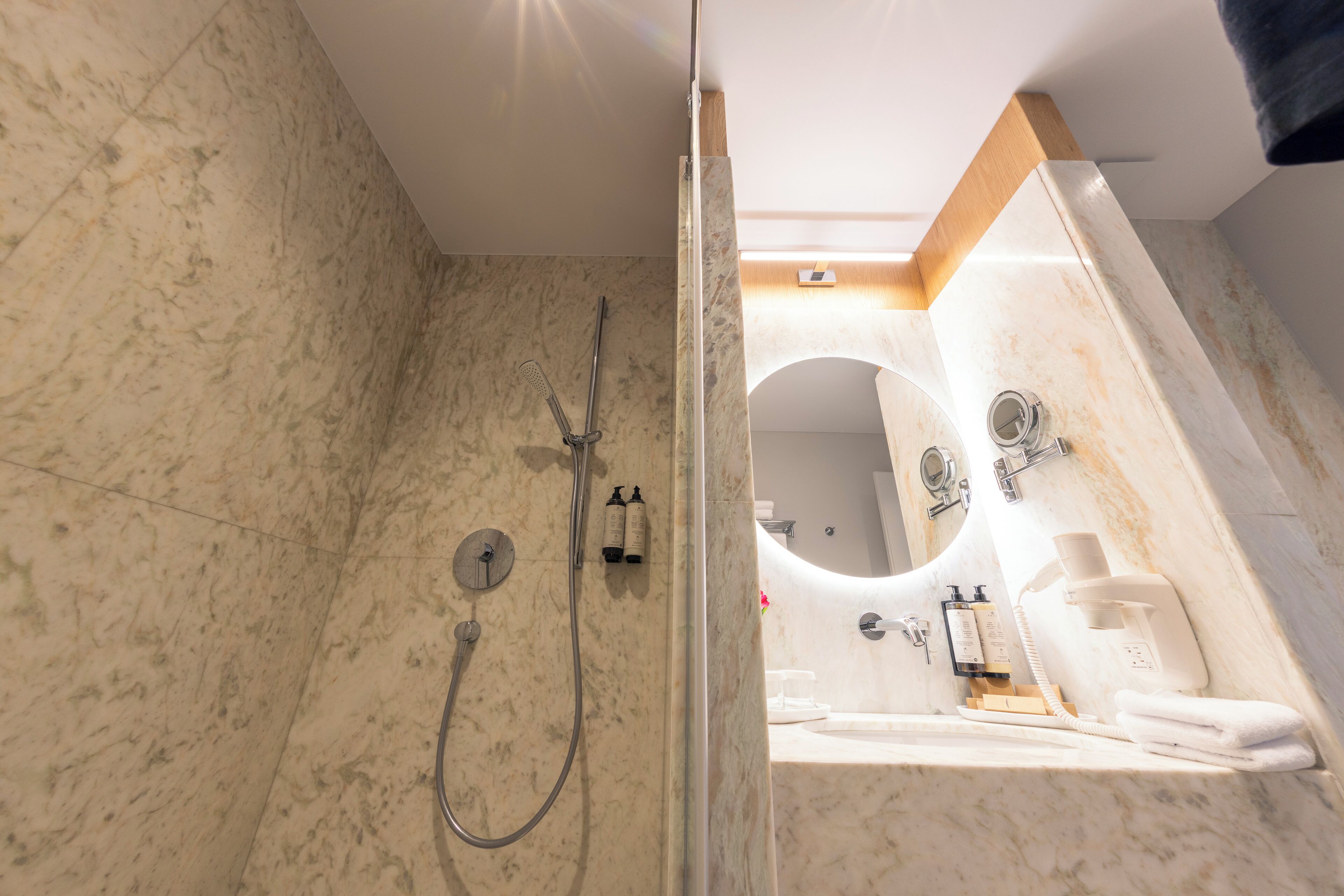 A modern bathroom with a marble floor, a glass-enclosed shower, a sink with a mirror, and toiletries.