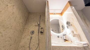 A modern bathroom with a marble floor, a glass-enclosed shower, a sink with a mirror, and toiletries.
