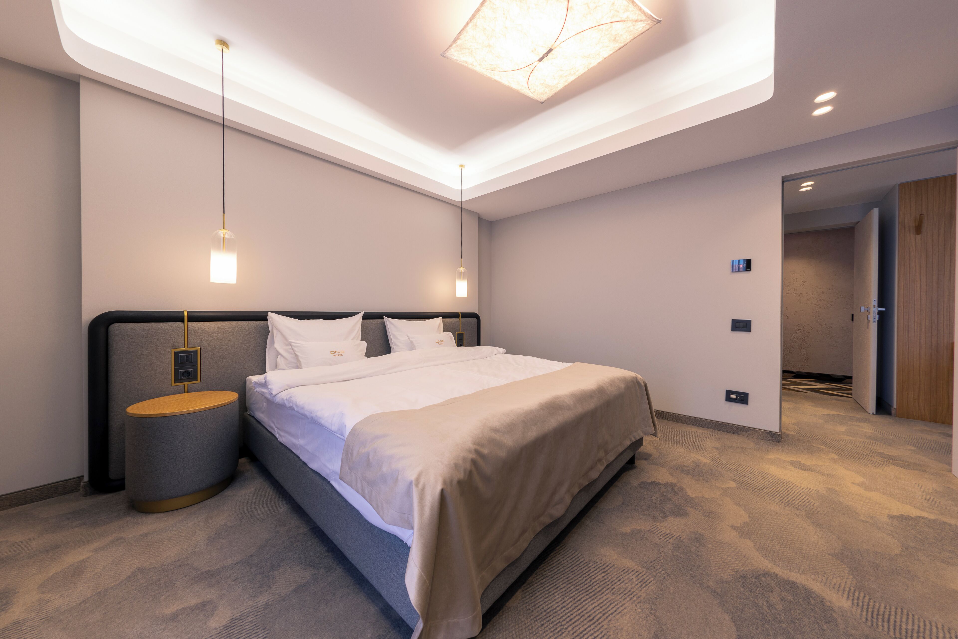 A modern hotel room with a large bed, a bedside table, a lamp, and a ceiling light.