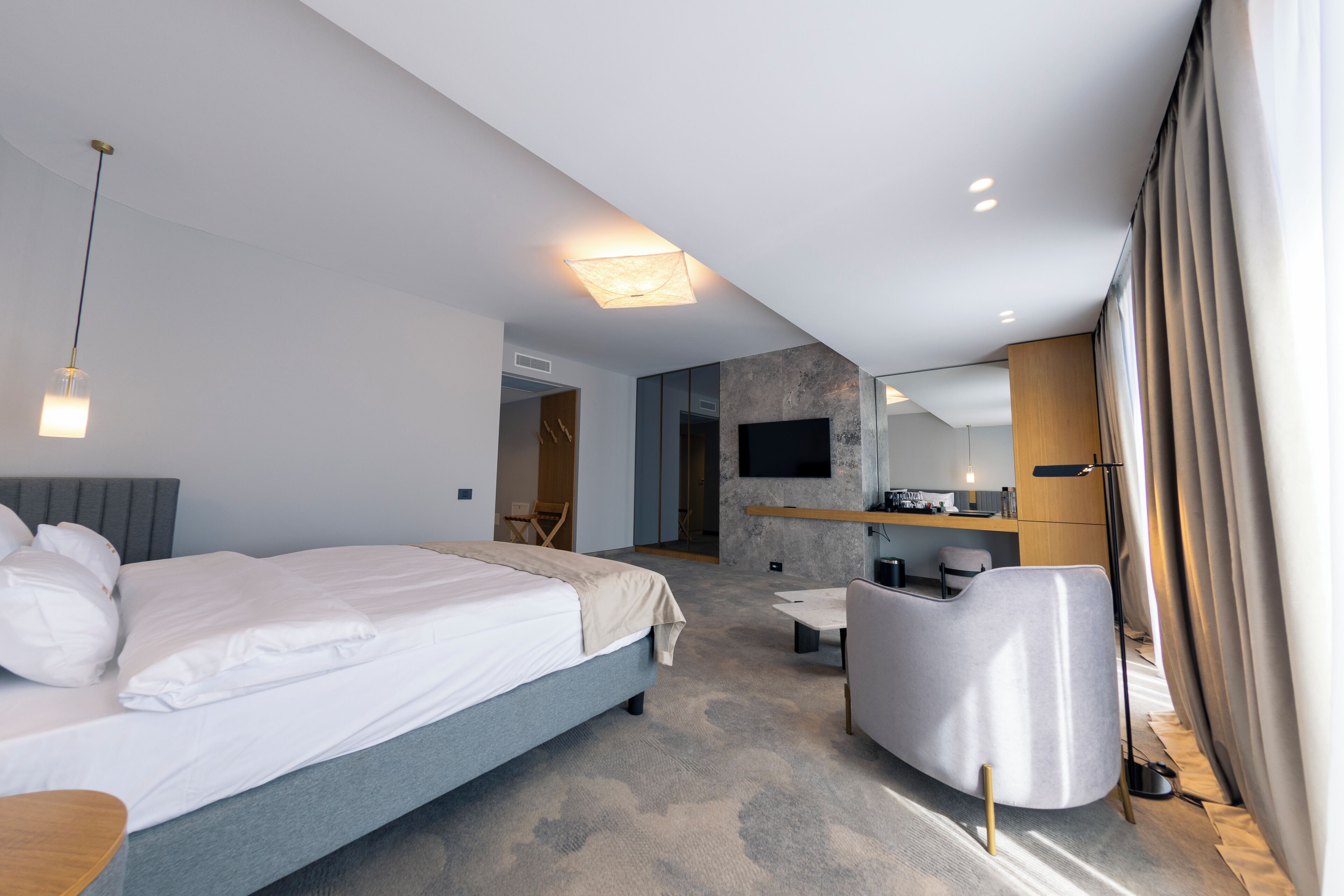 A modern hotel room with a large bed, a desk, a chair, and a TV.