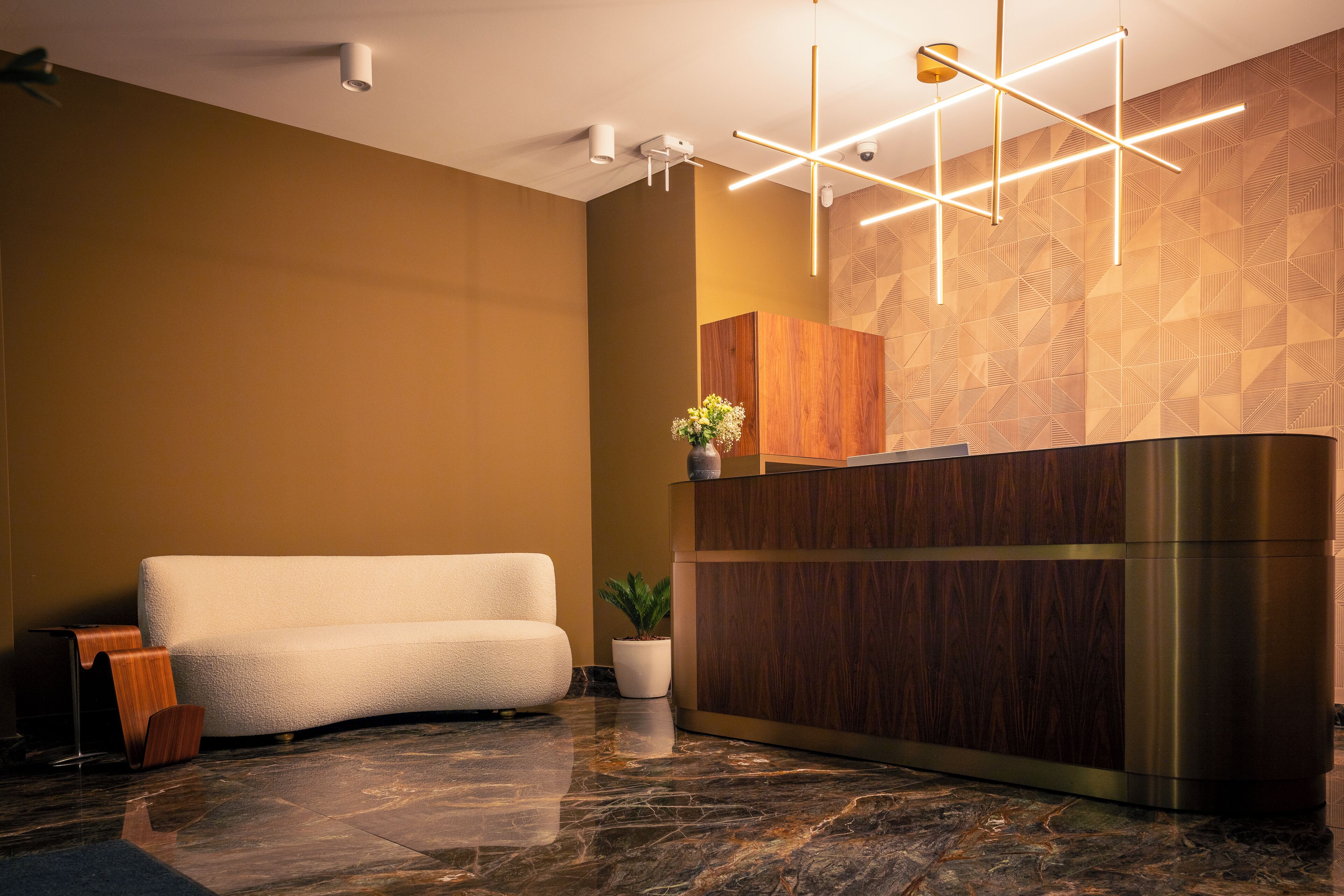 Un área de recepción con un mostrador de madera, un sofá blanco, una planta en maceta y una lámpara moderna.
