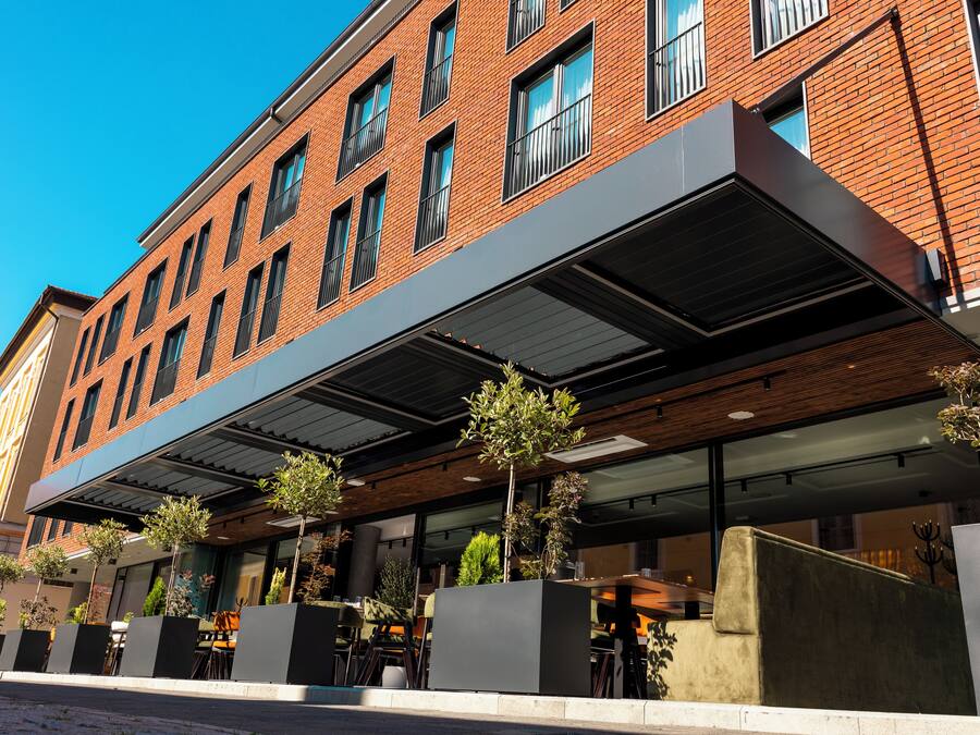Een modern gebouw met een bakstenen gevel, grote ramen en terras met plantenbakken.