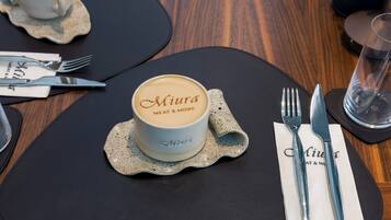 Une table dressée avec une tasse à café portant l’inscription « Miura Meat & More », des couverts et un verre d’eau.
