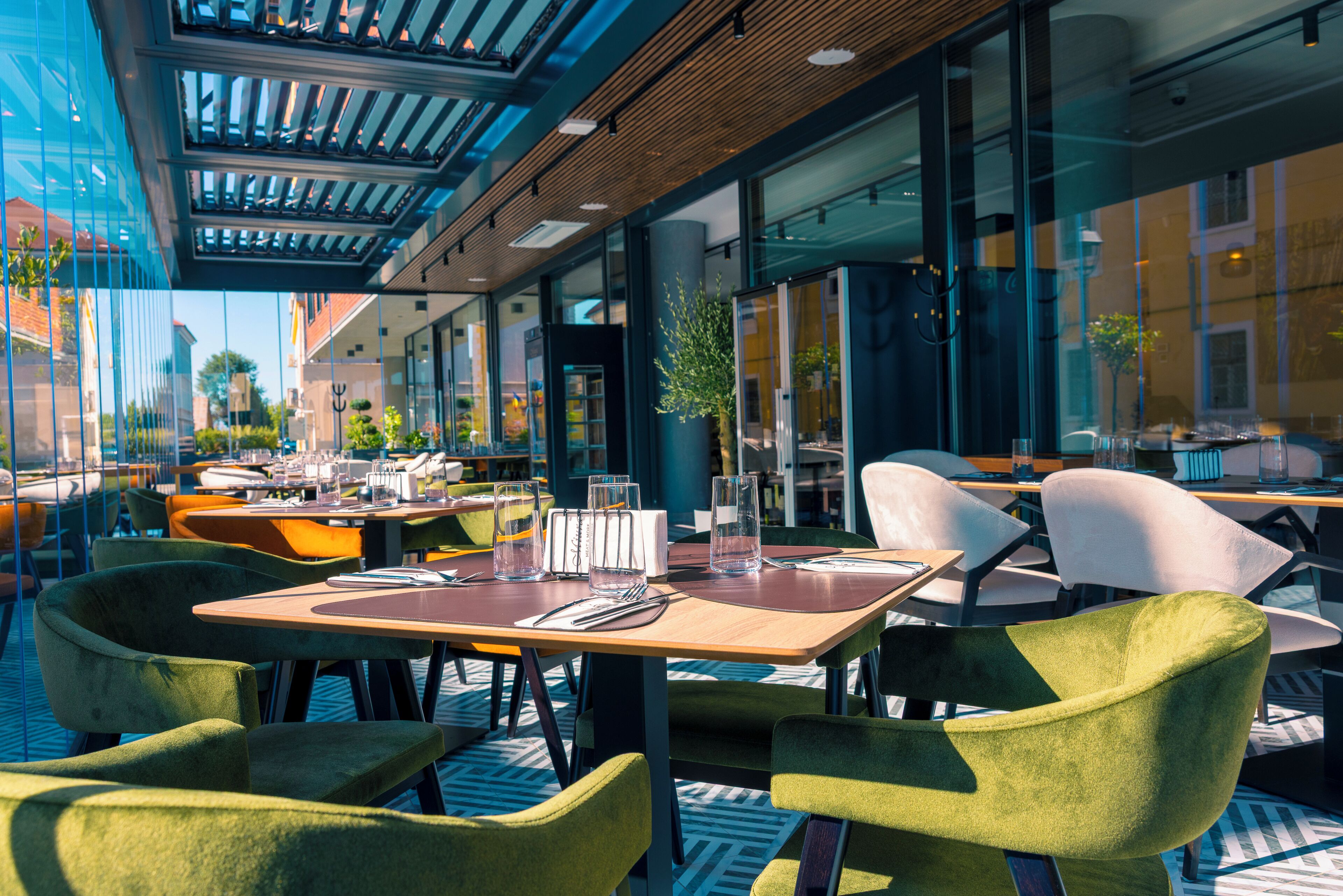 An outdoor dining area with tables and chairs, large windows, and a view of the city.