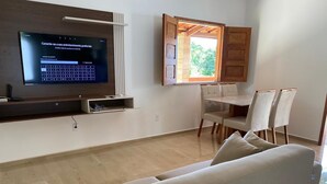 Een moderne woonkamer met een flatscreen televisie, een eethoek met een tafel en stoelen, en een bank.