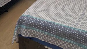 Een kamer met twee eenpersoonsbedden, een houten raam met luiken en een plafondventilator.