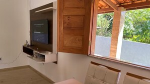 Een moderne eetruimte met een witte tafel en gestoffeerde stoelen, een houten deur en een aan de muur bevestigde televisie.