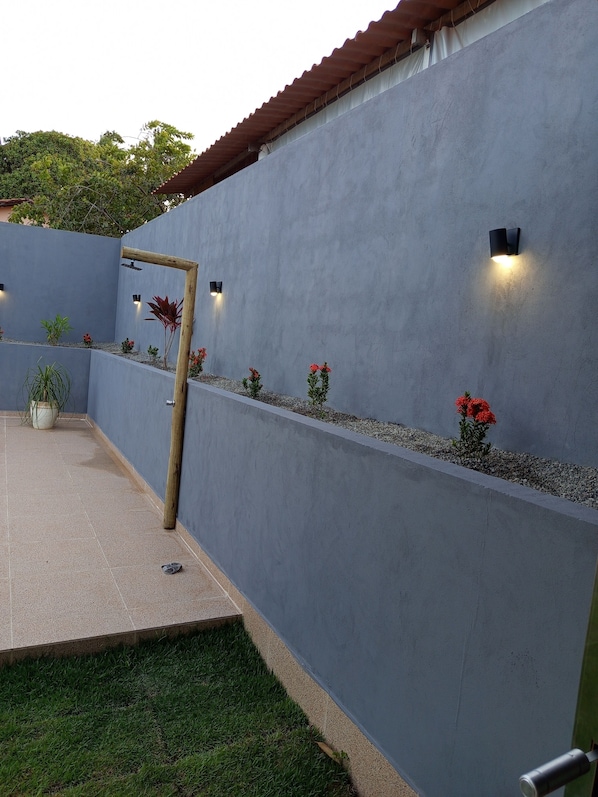 A modern outdoor patio with a concrete wall, potted plants, and a wooden pergola.