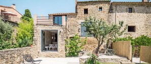 A stone building with a glass door entrance, outdoor seating, and a wooden fence. - Villa Sant Pere - Four Bedroom Apartment, Sleeps 8 (Vilopriu)