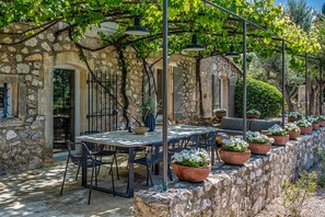 An outdoor dining area with stone walls, tables, chairs, and potted plants. - Maison De Bois - Five Bedroom Villa, Sleeps 10 (Maussane-les-Alpilles)