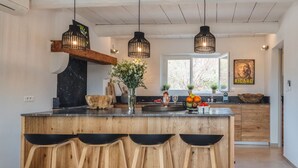 Een moderne keuken met een centraal eiland, houten krukken, hanglampen en een rustieke houten plank.