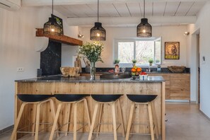 Eine moderne Küche mit Kochinsel, Holzstühlen, Pendelleuchten und einem rustikalen Holzbodenregal.