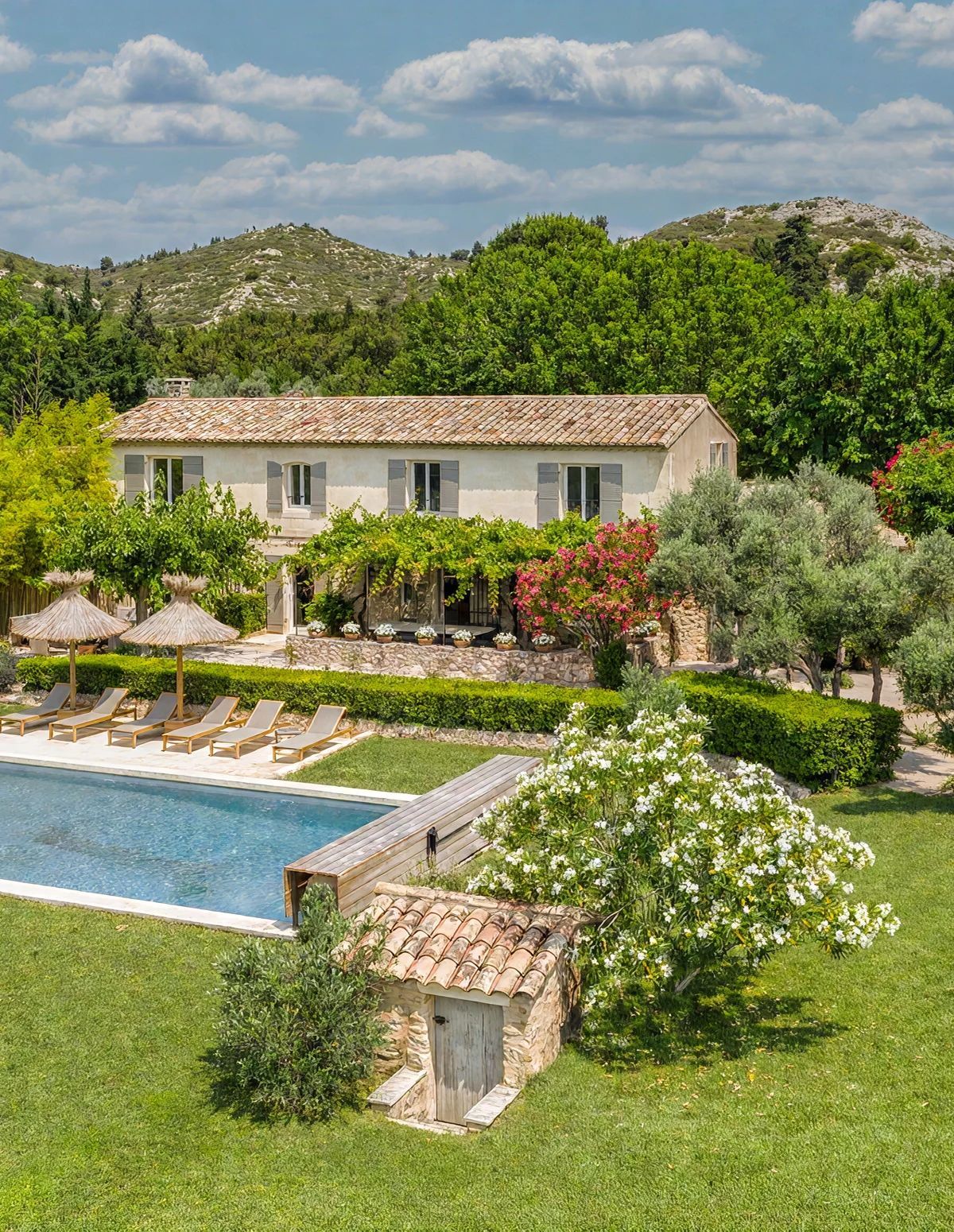 A villa with a swimming pool, a garden with a pergola, and a view of the surrounding hills.