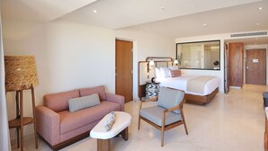 Una habitación de hotel moderna con sofá, una silla, una mesita, una cama y un espejo grande.
