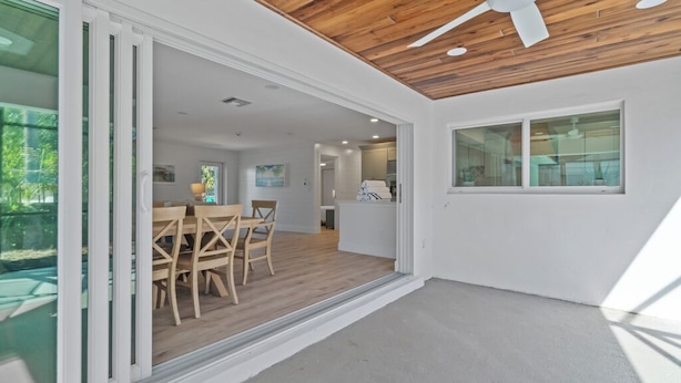 Un interior moderno con techo de madera, zona de comedor con mesa y sillas, y vista a un espacio exterior a través de puertas de vidrio.