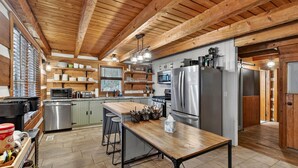 A spacious kitchen with wooden beams, stainless steel appliances, and a central island with bar stools. - Waterfront cabin w/fireplace, hot tub & BBQ grill (Maurertown)