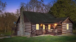 A log cabin with a stone chimney, wooden porch, and a small deck. - Waterfront cabin w/fireplace, hot tub & BBQ grill (Maurertown)