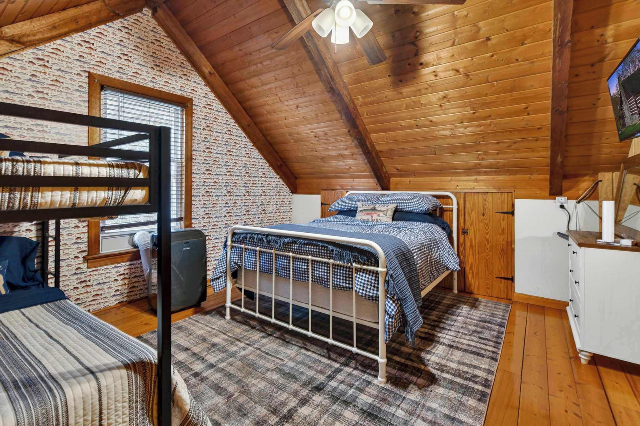 A cozy attic bedroom with a bunk bed, a single bed, a small desk, and a television.