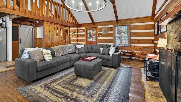 A cozy cabin interior with a large gray sectional sofa, a fireplace, and wooden paneling. - Waterfront cabin w/fireplace, hot tub & BBQ grill (Maurertown)