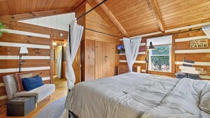 A cabin interior with a bed, a sofa, a lamp, and a window with curtains. - Waterfront cabin w/fireplace, hot tub & BBQ grill (Maurertown)