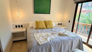 Une chambre à coucher avec un lit, des tables de chevet, un ventilateur de plafond et une vue sur l’extérieur.