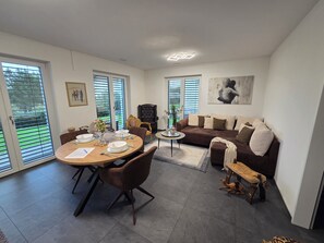 A modern living room with a dining area, large windows, and a sofa. - VIP Apartment (Böttstein)