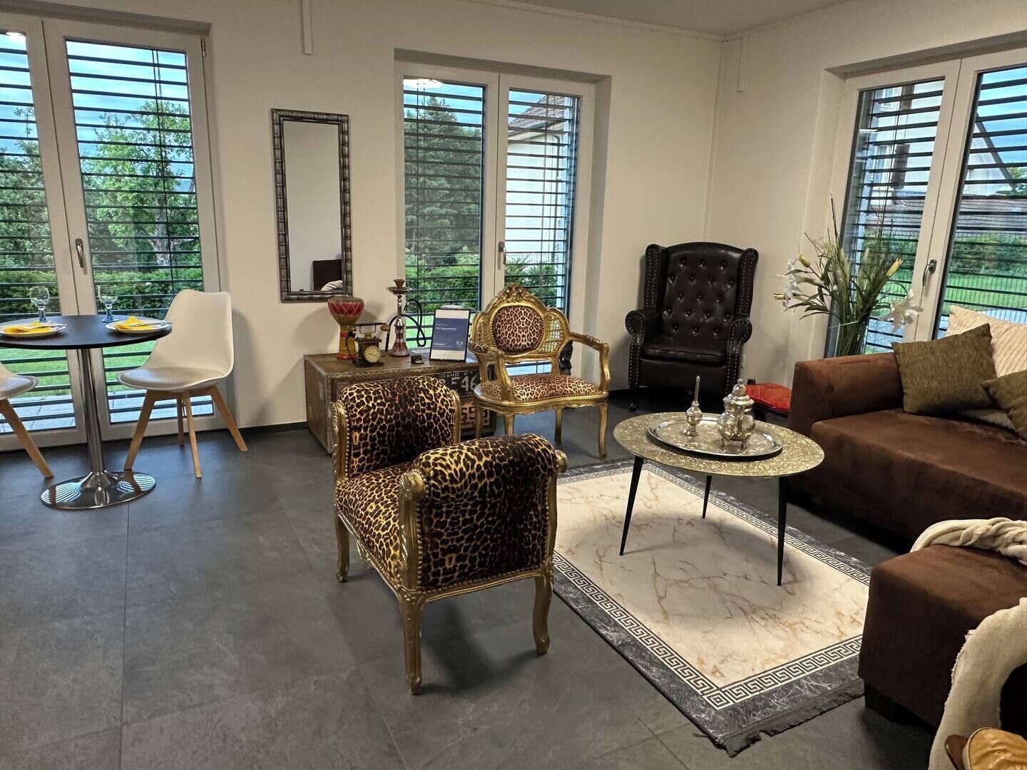 Una sala de estar con un sofá, dos sillones de estampado de leopardo, un sillón de cuero negro, una mesita redonda con una bandeja y una mesa de comedor con sillas.