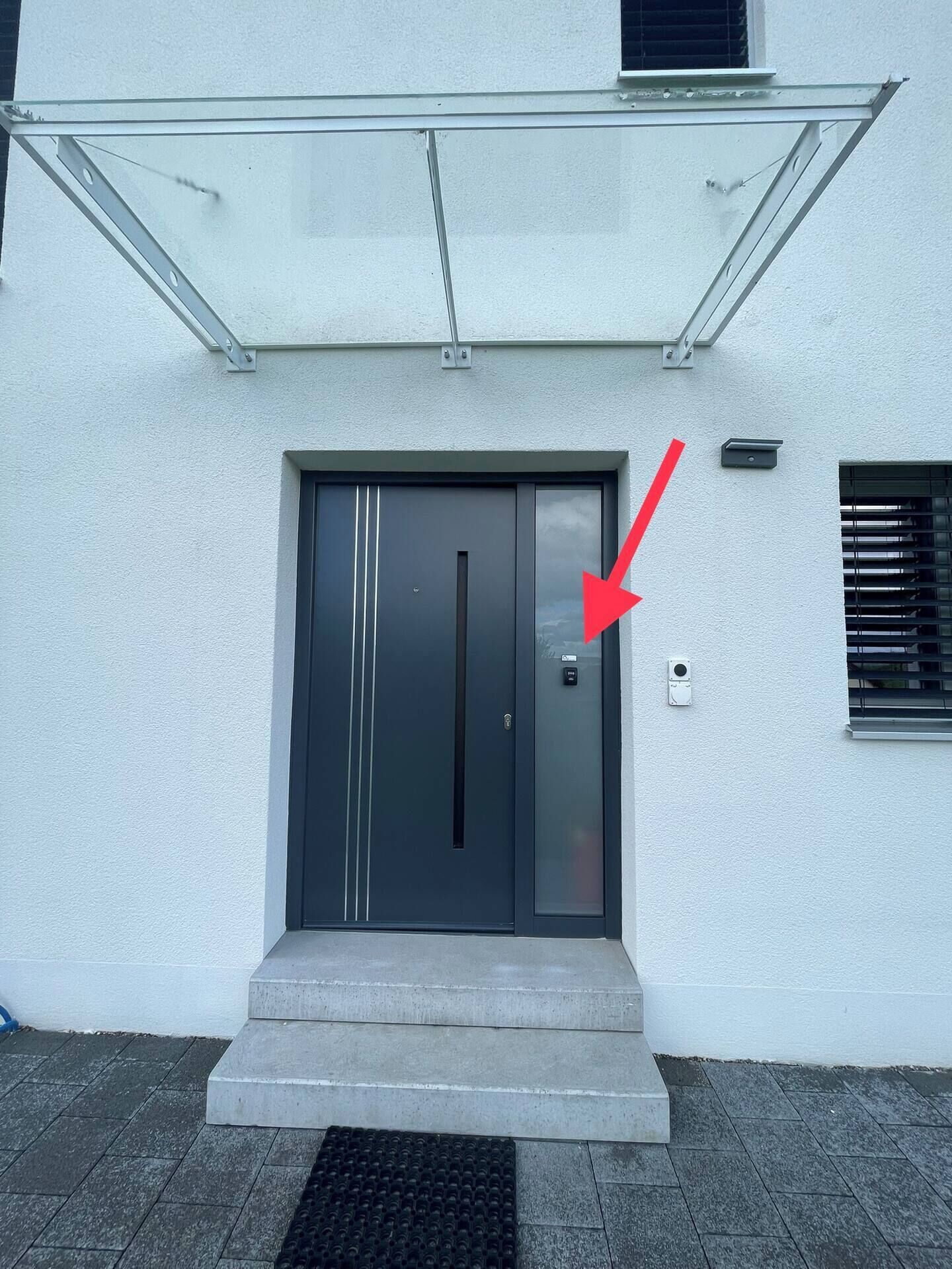 Un edificio moderno con una porta d'ingresso scura, un ingresso in vetro e una piccola finestra con persiane.