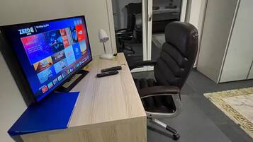A modern office space with a desk, chair, and a television displaying a streaming service interface.