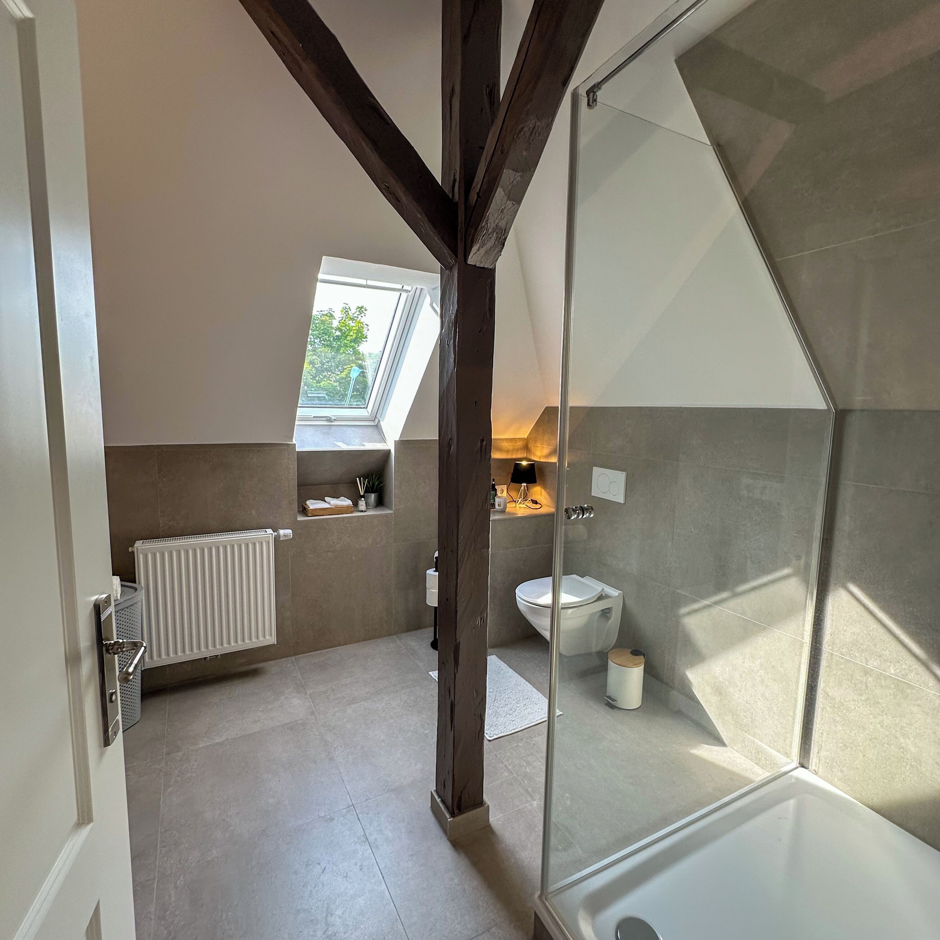 Ein modernes Badezimmer mit Duschkabine aus Glas, Dachfenster, Toilette und kleinem Fenster.