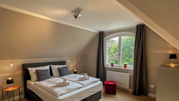 Un dormitorio moderno con una cama grande, una mesita de noche con lámpara, una ventana con cortinas y vistas a zonas verdes.