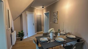 Un comedor con una mesa dispuesta para cuatro, sillas, un florero con flores y una botella de vino.