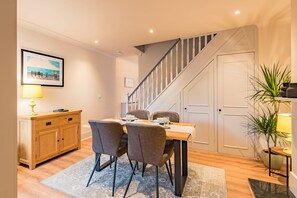 Un comedor con una mesa de madera, cuatro sillas, un mueble pequeño y una escalera.